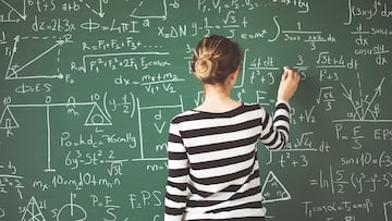 Young student writing with chalk on green chalk board in classroom