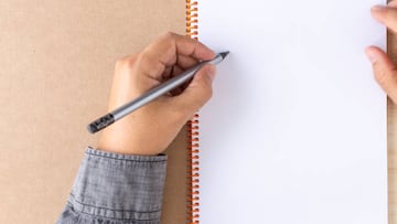 left-handed male with a pencil on the first white page of a spiral bound notebook