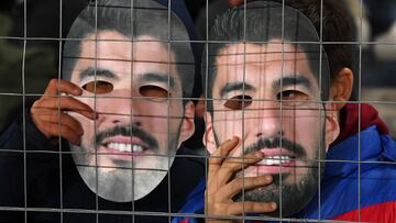 Fans of Nacional hold masks with an image of Uruguayan football star Luis Suarez during a campaign to try to convince him to return to the club, before the start of the Uruguayan First Division match between Nacional and Cerrito at the Gran Parque Central stadium in Montevideo on July 21, 2022. - A massive campaign on social networks has expanded in Uruguay so that the Uruguayan idol Luis Su�rez returns to Nacional, the club of his beginnings before acquiring world fame. Under the hashtag #Su�rezANacional, fans of Nacional are trying to convince him to join the club until the World Cup. (Photo by Pablo PORCIUNCULA / AFP)