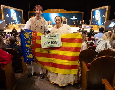 Una pareja vestidos con el traje de fallera y una bandera de la Comunidad Valenciana durante la celebración del Sorteo Extraordinario de la Lotería de Navidad 2024.