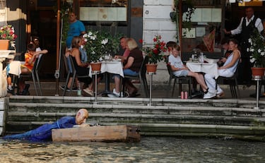 Personas observan la instalación de un maniquí que representa al fundador de Amazon, Jeff Bezos, en una balsa hecha con cajas de Amazon flotando en el agua.