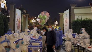 A child holds Mickey Mouse balloons as visitors receive COVID-19 tests at the Shanghai Disney Resort in Shanghai, China on Sunday, Oct. 31, 2021. Fireworks boomed as the visitors at Shanghai Disneyland waited for their COVID-19 test results, surrounded by healthcare workers dressed from head to toe in the white protective suits. Shanghai Disneyland suddenly announced Sunday evening that they were no longer accepting any visitors and they were cooperating with an epidemiological investigation from another province. They then locked down the park, as Shanghai city healthcare workers and police rushed to the scene to conduct a mass testing. (Chinatopix via AP)
