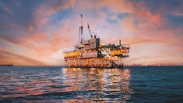 A stunning sunset photo showcases offshore oil drilling in Huntington Beach, California, with vivid hues casting a glow on industrial equipment
