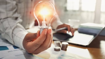 business woman hand holding lightbulb with coins stack on desk. concept saving energy power