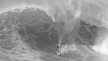 Imagen en blanco y negro de una ola gigante en Nazaré (Portugal), con un surfista.