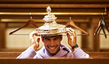 Carlos Alcaraz posa sonriente, en el interior del vestuario, con el trofeo de campeón del torneo de Queen’s sobre su cabeza. El tenista murciano se proclamó campeón del torneo londinense por segunda vez, tras superar en la final al checo Jiri Lehecka. Su proxima cita, también en la hierba londinense, será en el All England Club, en Wimbledon. 