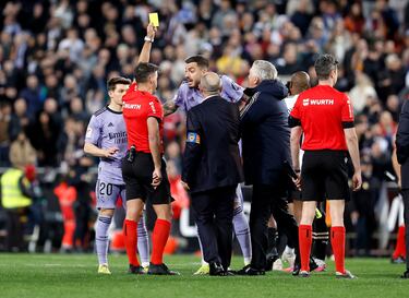 Los jugadores del Real Madrid protestan al árbitro del encuentro, Gil Manzano, tras la decisión de anular el gol a Jude Bellingham. En la imagen, el colegiado muestra la cartulina amarilla a Joselu.