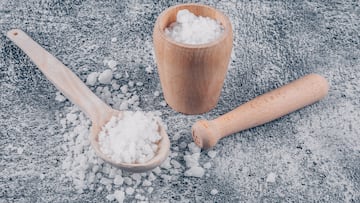 Sea salt in a bowl and spoon with rolling pin high angle view on a gray textured background