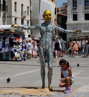 Un niño se arrodilla junto a un maniquí que representa al fundador de Amazon, Jeff Bezos, cubierto de billetes falsos, instalado en la Plaza de San Marcos como parte de una parodia del colectivo artístico Konn Artiss, antes de la boda de Bezos y la periodista Lauren Sánchez.