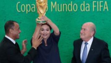 La presidenta de Brasil, Dilma Rousseff, sostiene el trofeo de la Copa del Mundo, junto al presidente de la FIFA, Joseph Blatter, y exjugador brasileño Cafú.