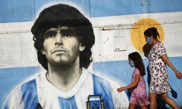 A woman and a girl walk by a mural of Diego Maradona (BA)