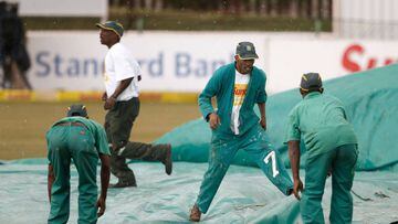 Field marshals and workers run to cover the pitch as rain starts during the fourth day of the first Test cricket match between South Africa and Bangladesh in Potchefstroom on October 1, 2017. / AFP PHOTO / GIANLUIGI GUERCIA