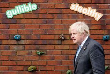 British Prime Minister Boris Johnson passes by a wall with the words "gullible" and "stealthy" during his visit to St Mary's CE Primary School, ahead of reopening of the primary and secondary schools across England planned for March 8, in Stoke-on-Trent, 