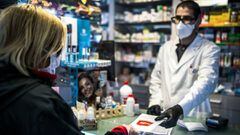 Un farmaceutico entrega la mascarilla a una cliente en una farmacia.
