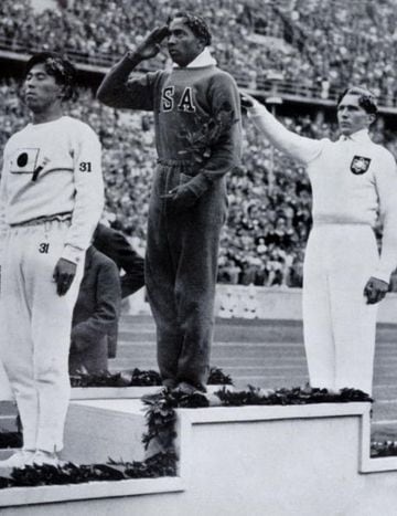 Jesse Owens en el podio olímpico después de su victoria en el salto de longitud en los Juegos Olímpicos de Berlín 1936 junto a Naoto Tajima (izquierda) y Luz Long (derecha). El la entrega de la cuarta medalla de oro a Owens, Hitler se limitó a abandonar el estadio para no verse obligado a estrechar la mano del atleta negro. 