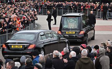 Los asistentes presentan sus respetos mientras pasa el coche fúnebre que transporta el ataúd.