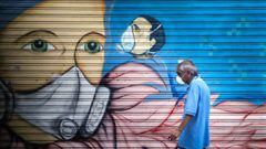 Un hombre con mascarilla pasa frente a un mural en Buenos Aires (Argentina). EFE/Juan Ignacio Roncoroni