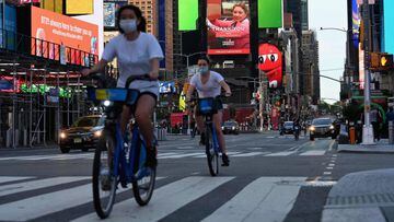 (FILES) In this file photo taken on May 27, 2020 people wearing a facemasks ride their bikes through Times Square in New York City, amid the novel coronavirus pandemic. - New York, the US city worst-hit by the coronavirus, is &quot;on track&quot; to start