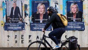 A man rides a bike in front of posters of Marine Le Pen, French far-right National Rally party candidate for the 2022 French presidential election.