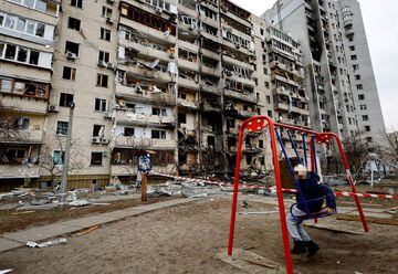 A child sits on a swing opposite a Kyiv residential building badly damaged by a Russian assault.