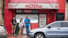 A family wearing facemasks stands in front of a pizzeria in Austin, Texas, June 26, 2020. - Texas Governor Greg Abbott ordered bars to be closed by noon on June 26 and for restaurants to be reduced to 50% occupancy. Coronavirus cases in Texas have spiked 