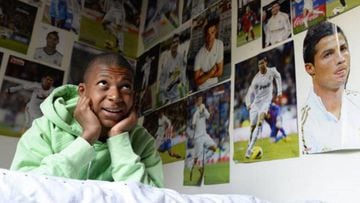 A young Kylian Mbappé poses with posters of Cristiano Ronaldo in his room.