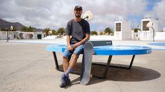 Marcos &Aacute;lvarez sentado en una mesa de Teqball (f&uacute;tbol y ping pong) en las Islas Canarias, con la tabla de skate apoyada en la misma, una pista de baloncesto al fondo y un cielo nublado. 