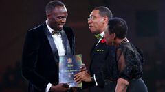 Usain Bolt recibe un premio de manos del primer ministro jamaicano, Andrew Holness y de la ministra de Cultura y Deporte, Olivia Grange.