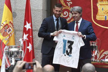 El defensa y capitán del Real Madrid, Sergio Ramos, entrega una camiseta conmemorativa al presidente de la Comunidad de Madrid, Ángel Garrido.