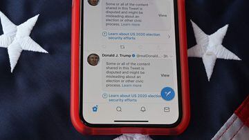(FILES) In this file photo taken on November 05, 2020 shows a mobile phone placed on a US flag with Tweets from US President Donald Trump masked with warnings imposed by Twitter stating that they may be incorrect. - Twitter labeled 300,000 tweets related 