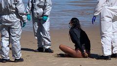 Una surfista sentada y esposada en la playa de la Zurriola (San Sebasti&aacute;n), con 3 miembros de la Ertzaintza equipados con EPIs, ya que la chica se puso a surfear a pesar de tener el coronavirus. 