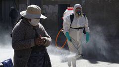 A municipal worker sprays disinfectant past a street vendor at a market in Puno, Peru, near the border with Bolivia, on June 10, 2020. - The inhabitants of the Andean heights of Bolivia and Peru have resisted the new coronavirus better than their compatriots of the low lands, which has called experts&#039; attention. (Photo by Carlos MAMANI / AFP)