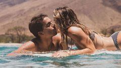 Kai Lenny y Molly Lenny d&aacute;ndose un beso en el agua sobre una tabla de surf. 