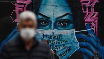People wear face masks near a mural depicting a woman wearing a face mask in Bogota on April 14, 2021, amid the COVID-19 pandemic. - Colombia announced the confinement of 12 million people against a third wave of covid-19. (Photo by Juan BARRETO / AFP)