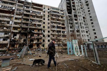 A man walks a dog in front of a Kyiv residential building badly damaged by Russian military action against the city.