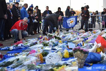 A Liverpool football club supporter (L) adds to flowers to a growing pile of tributes outside Leicester City Football Club's King Power Stadium