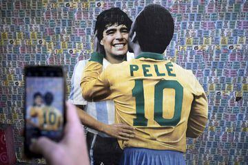 Un hombre toma una foto a la pintura mural en Buenos Aires, en la que el artista reflejó un saludo entre las dos grandes estrellas del fútbol ya fallecidas, Maradona y Pelé, como si se hubiesen enfrentado en un terreno de juego.