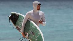 El bicampe&oacute;n del mundo de surf, paseando con su tabla por la playa y con una camiseta con capucha para protegerse del sol. 