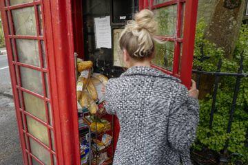 A woman collects food from a disused traditional red phone box, now converted into a free community foodbank by local residents in Carrbrook Village, Manchester.