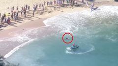 Un delf&iacute;n (con c&iacute;rculo rojo) a punto de morir en la orilla de Shelly Beach, en Manly, Australia, con un jet ski y varios espectadores y surfistas mirando, el s&aacute;bado 21 de enero del 2023. 