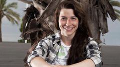 Anna Kruse sonriendo y posando sobre su tabla de skate, ante una palmera. 