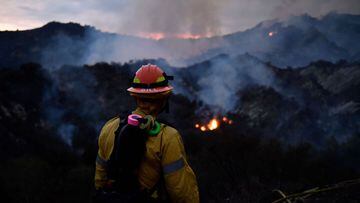 A firefighter watches the flames from the Palisades fire glow in the distance in Topanga State Park, North West of Los Angeles on May 15, 2021. - A brush fire near Pacific Palisades started Friday and grew to 750 acres Saturday night, triggering a mandatory evacuation of residents in the Topanga area. (Photo by Patrick T. FALLON / AFP)