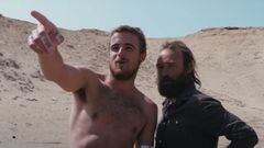 Natxo Gonzalez se&ntilde;ala una ola con el dedo mientras Kepa Acero se la mira, con dunas del desierto detr&aacute;s, en un viaje de surf a &Aacute;frica durante el 2022. 