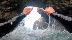 Los brazos y manos de Guillermo Carracedo realizando el saludo surfero del shaka bajo los arcos de roca de la playa de las Catedrales (Galicia, Espa&ntilde;a). 
