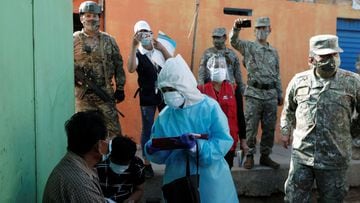 Soldiers keep watch as a healthcare worker wearing personal protective equipment (PPE) talks to a man in Cantagallo, an indigenous Shipibo-Conibo community, during the vaccination campaign against the coronavirus disease (COVID-19), in Lima, Peru February 19, 2021. REUTERS/Angela Ponce