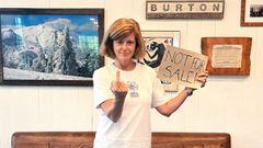 La presidenta de Burton Snowboards, Dona Carpenter, sostiene un cartel de Not for sale con una mano y con la otra realiza una peineta. Frente a un sof&aacute; y unos cuadros. 