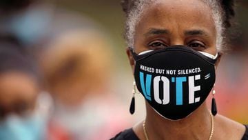 A woman wears a mask with a message urging voter participation while she waits in line to enter a polling place