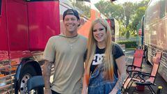 El skater Ryan Sheckler y la cantante Avril Lavigne sonriendo frente a unos autocares y unas sillas. 