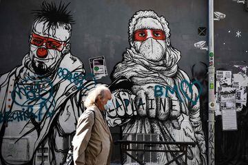 A man wearing a face mask walks past a graffiti in Marseille, southern France on April 25, 2020, as the country is under lockdown to stop the spread of the Covid-19 pandemic caused by the novel coronavirus.