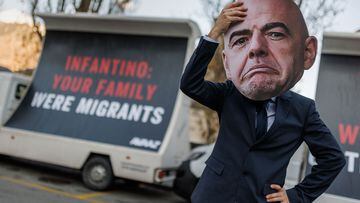 A man with a mask representing FIFA President Gianni Infantino gestures next to giant billboards in a street of Infantino's hometown of Brig, where his parents originally moved as migrants, during a protest by NGO Avaaz calling on Infantino to commit to a $440 million FIFA compensation fund for victims of this Qatar 2022 World Cup football tournament, on December 7, 2022. (Photo by VALENTIN FLAURAUD / AFP)